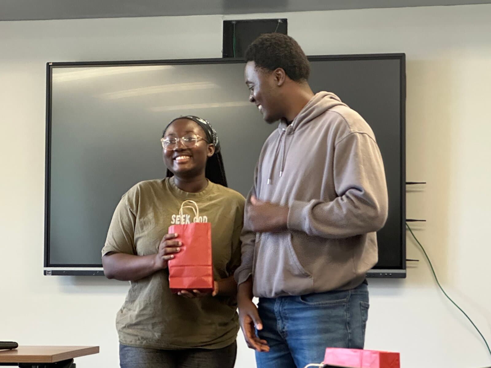 Joyful fellowship moment with a SEEK GOD shirt and red gift bag